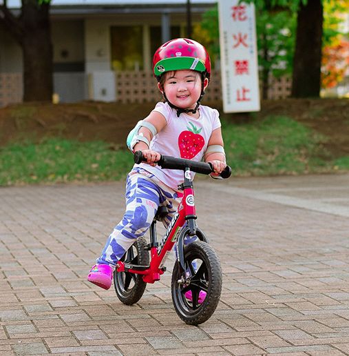 Girl smiles as she rides a red Strider Sport