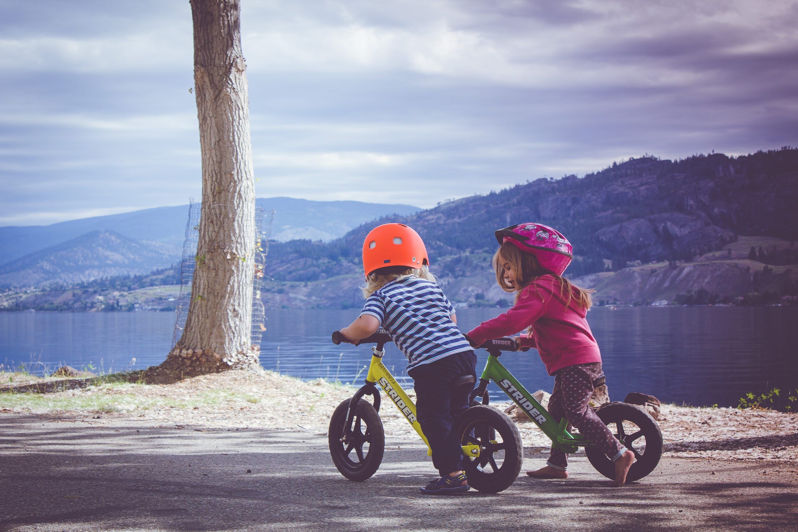 Boy and girl ride their bikes on a path next to a lake 