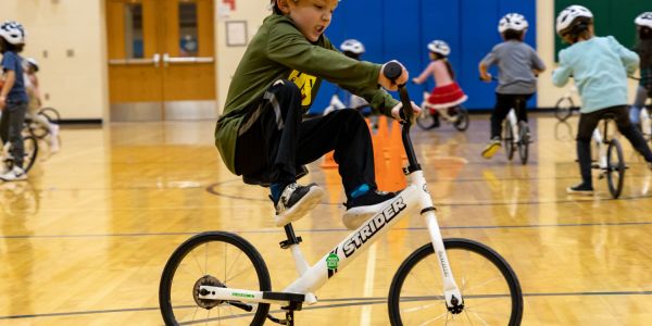 A boy lifts his feet and "glides" during the All Kids Bike Kindergarten PE Program