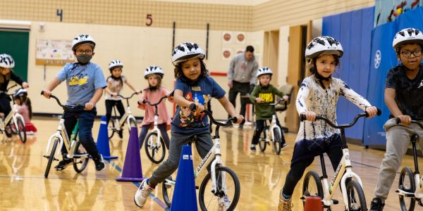 Kindergarteners on bikes weave through cones in a school gym