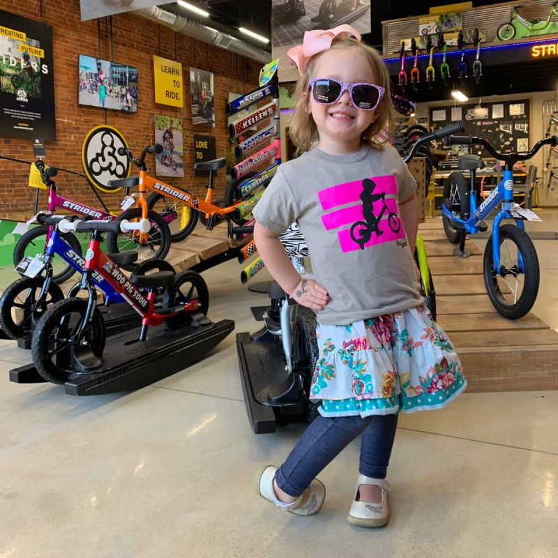 A young girl poses in front of a ramp full of Strider Bikes