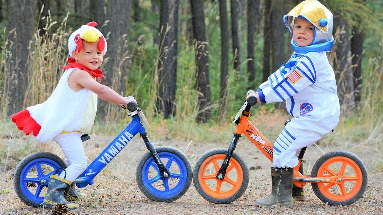 Two kids in costumes on Strider balance bikes with wheel colors that match their bikes