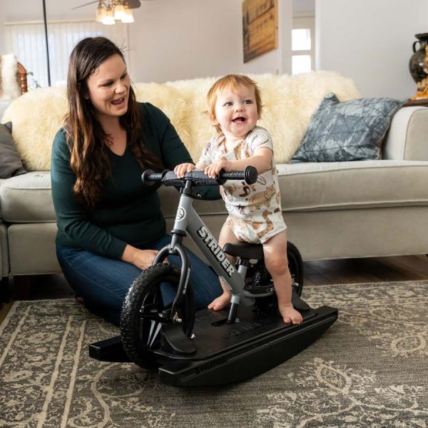 A smiling mom and baby play on a Strider rocking bike