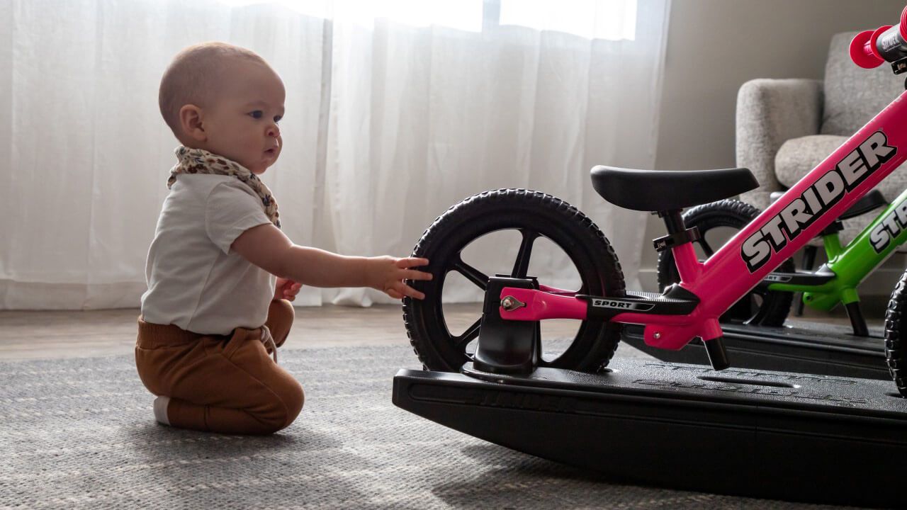 A baby checking out a pink Rocking Bike