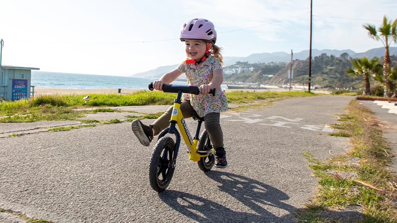 Girl gliding on 12-inch yellow Strider balance bike