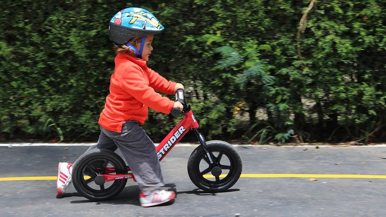 Toddler striding on red 12-inch Strider balance bike