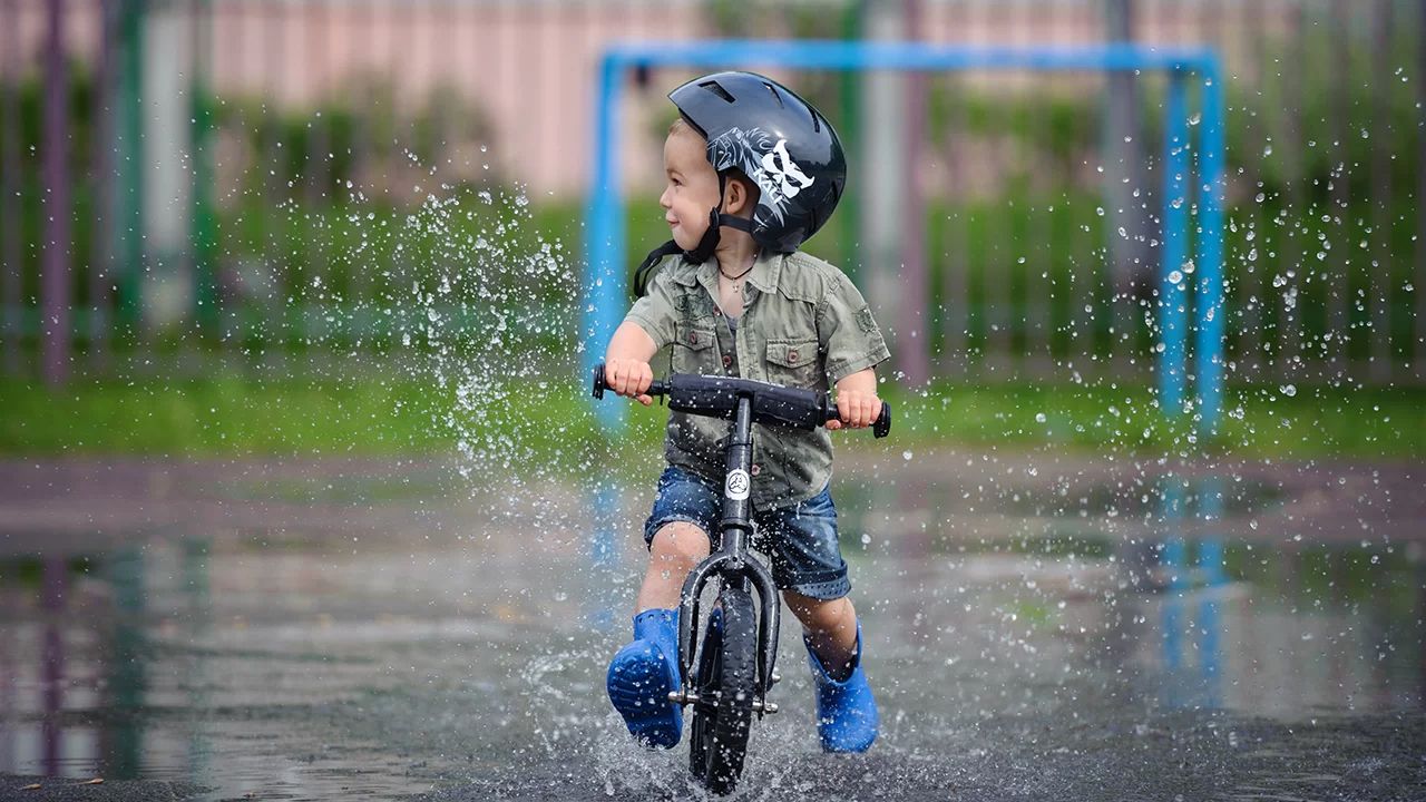 Toddler striding through water on black 12-in Strider balance bike