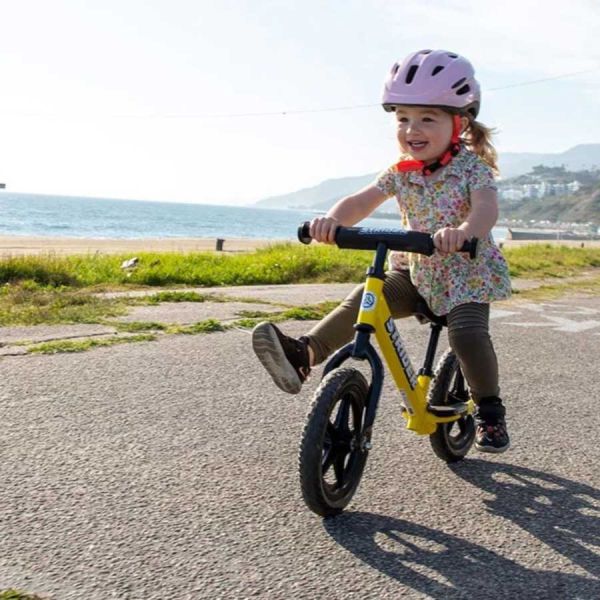 a girl rides a yellow Strider 12 Sport along a beach