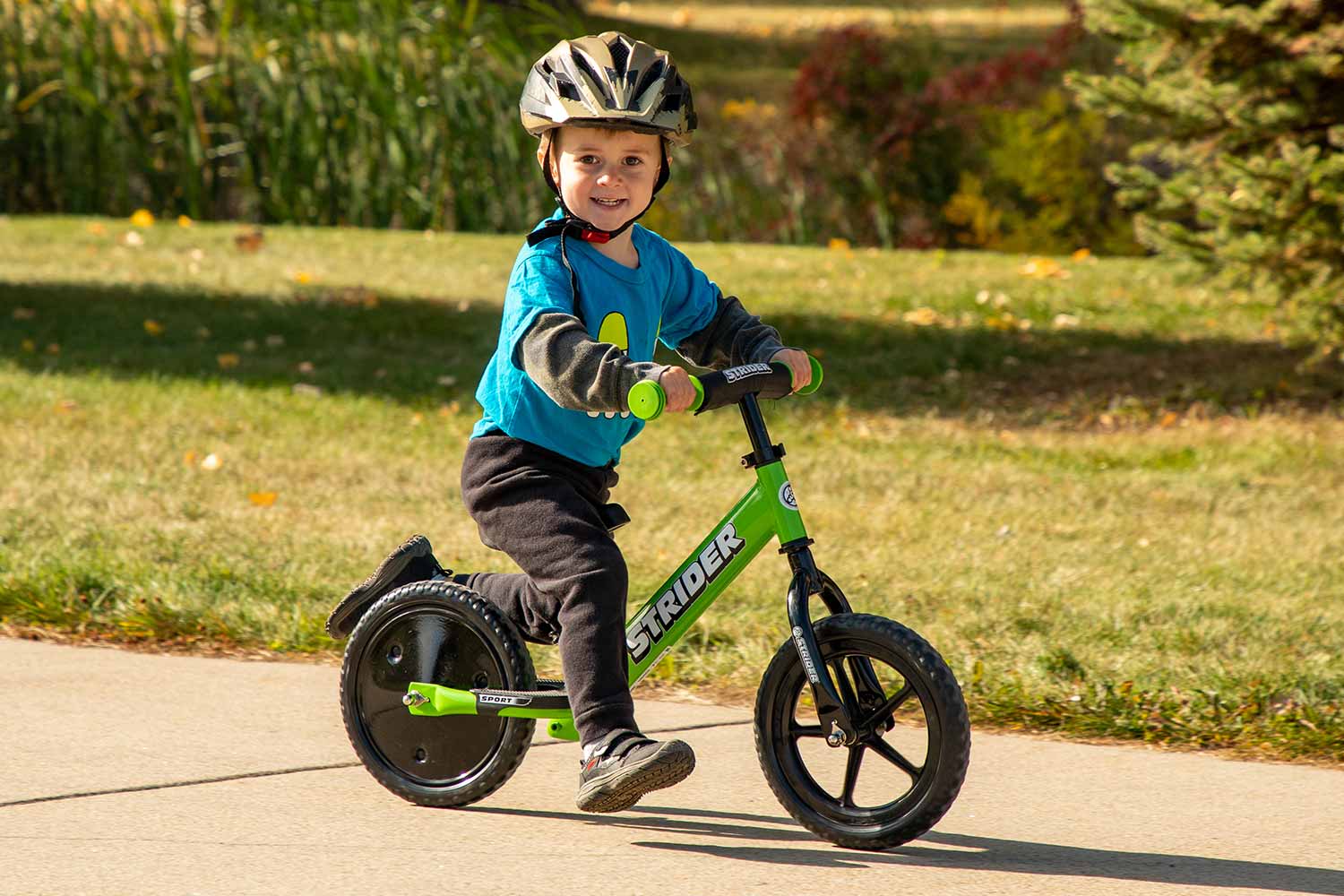 A boy riding a green Strider bike with a set of Disc Wheel Covers on the rear wheel